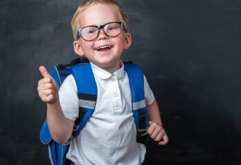 Happy Smiling Boy In Glasses With Thumb Up Is Going To School For The First Time. Child With School
